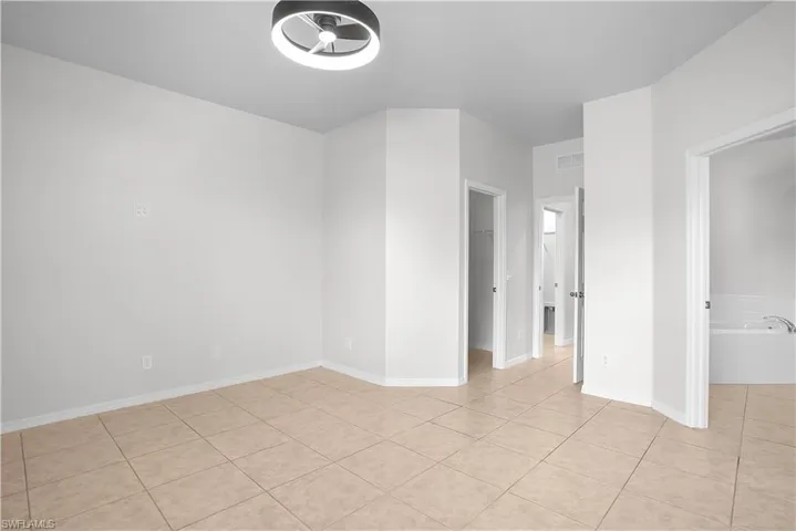 Spacious room featuring neutral-toned tile flooring, white baseboards, and a modern ceiling light fixture