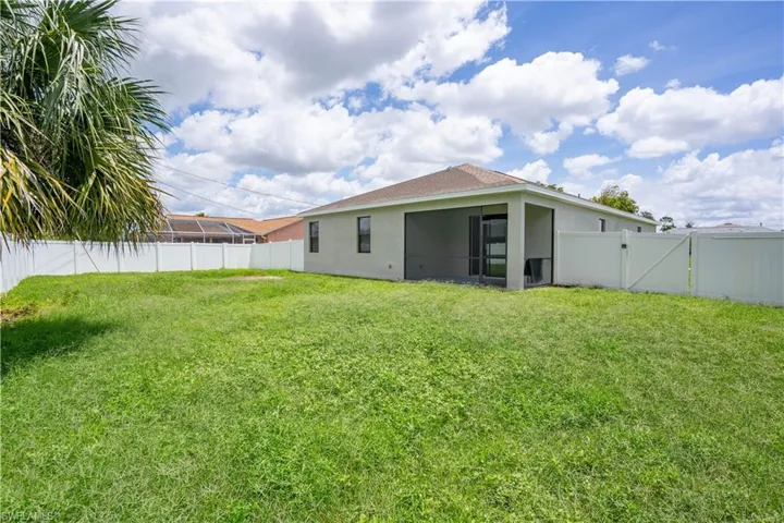 Expansive grassy backyard featuring a full privacy fence, screened patio, and a palm tree