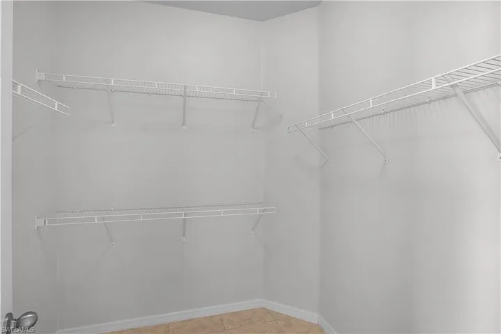 Spacious walk-in closet featuring light gray walls, white wire shelving, and a tiled floor