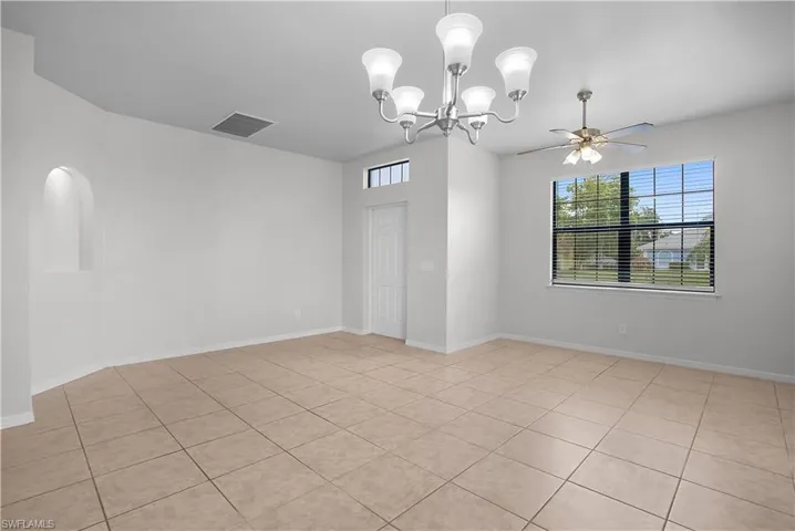 Spacious room featuring neutral tile flooring, a large window with horizontal blinds, and a decorative arched wall niche