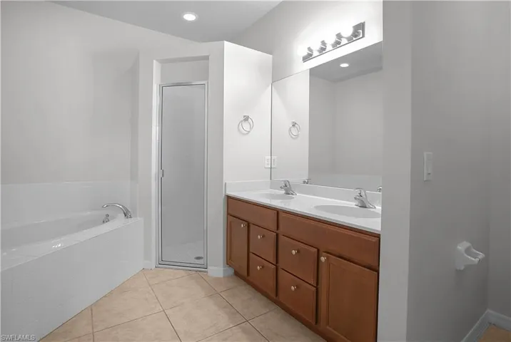Bathroom featuring a double vanity with wood cabinetry and white countertops, a large mirror, a separate shower with a glass enclosure, a built-in bathtub, and tile flooring