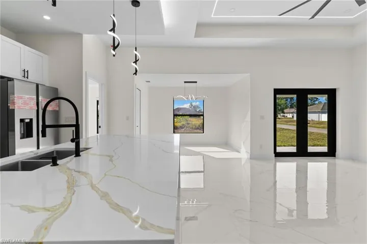 Kitchen with pendant lighting, light stone counters, stainless steel refrigerator with ice dispenser, light marble finish flooring, and white cabinets