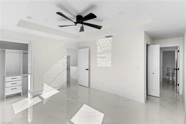 Unfurnished bedroom featuring a raised ceiling and light marble finish floors