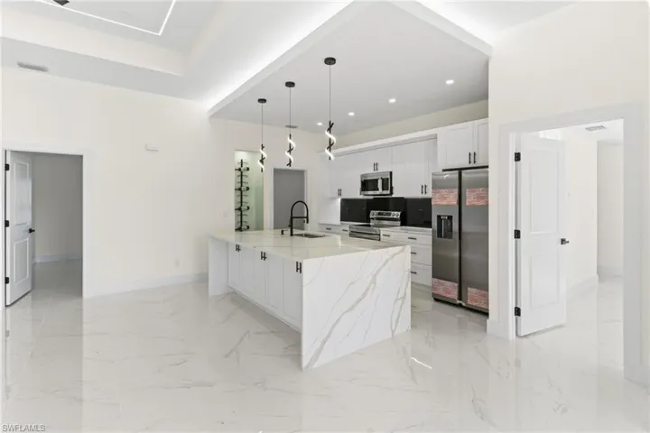 Kitchen featuring pendant lighting, white cabinets, stainless steel appliances, light stone counters, and light marble finish floors