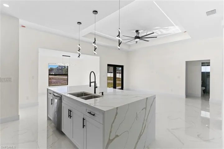 Kitchen featuring ceiling fan, a raised ceiling, healthy amount of natural light, and light stone counters
