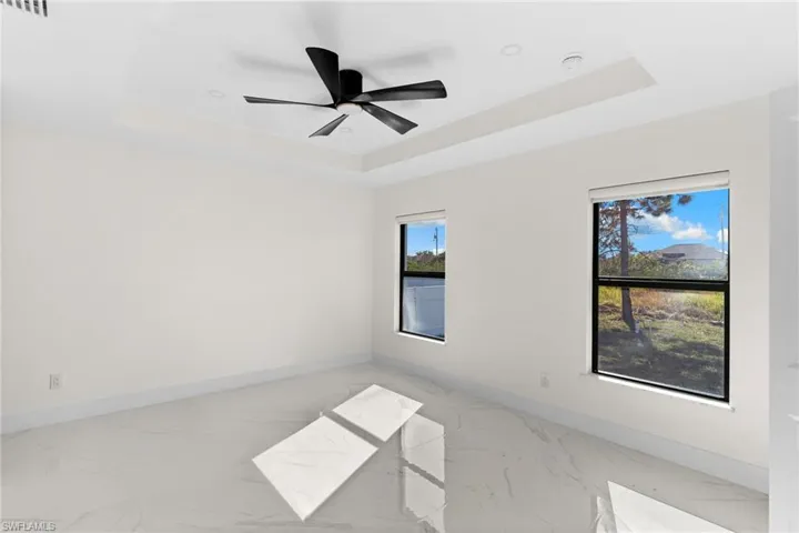 Spare room featuring a raised ceiling, light marble finish flooring, and a ceiling fan