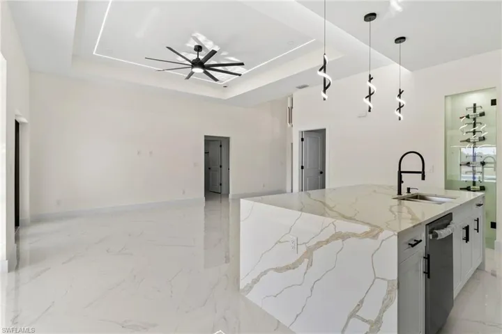 Kitchen with light stone counters, a center island with sink, pendant lighting, open floor plan, and white cabinetry