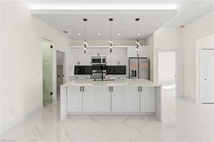 Kitchen with white cabinetry, light stone counters, appliances with stainless steel finishes, a large island with sink, and decorative light fixtures