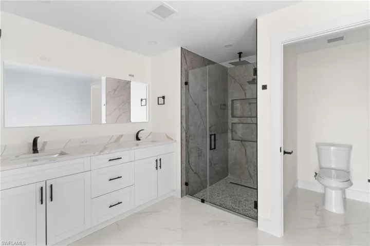Full bathroom with double vanity, a marble finish shower, and light marble finish flooring