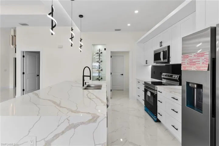 Kitchen with appliances with stainless steel finishes, white cabinets, light stone counters, pendant lighting, and recessed lighting