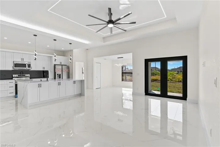 Unfurnished living room with a raised ceiling, a ceiling fan, light marble finish flooring, and a chandelier