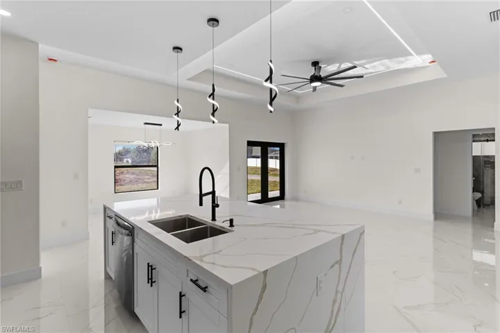 Kitchen featuring light stone countertops, a raised ceiling, decorative light fixtures, and a kitchen island with sink