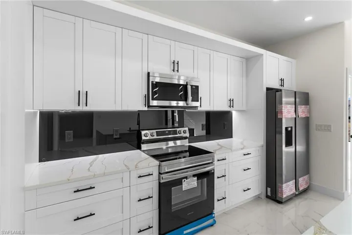 Kitchen with appliances with stainless steel finishes, light stone counters, white cabinets, light marble finish flooring, and recessed lighting