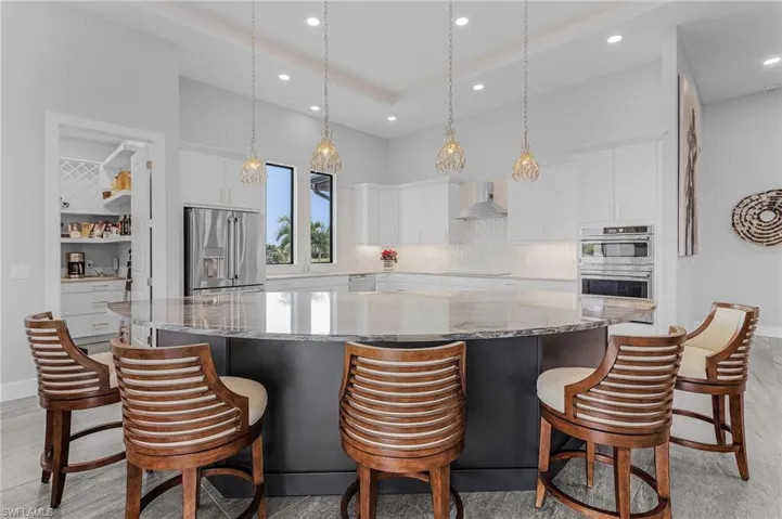 Kitchen with white cabinets, wall chimney exhaust hood, stainless steel appliances, and a large island