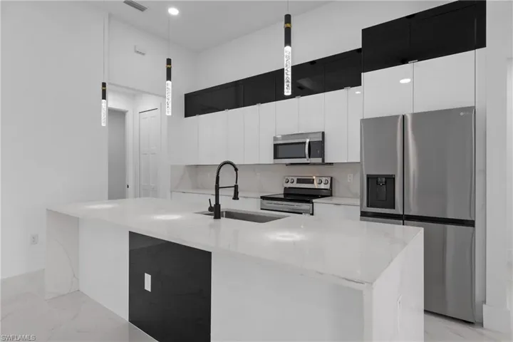 Kitchen with light stone counters, an island with sink, appliances with stainless steel finishes, sink, and decorative light fixtures