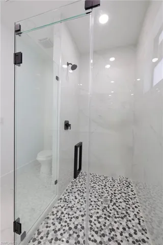 Bathroom with toilet, a shower with shower door, and tile patterned floors
