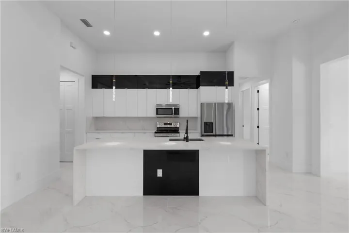 Kitchen featuring sink, a large island, white cabinetry, stainless steel appliances, and decorative light fixtures