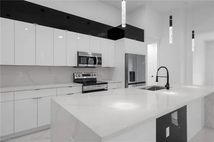 Kitchen with a large island, light stone counters, appliances with stainless steel finishes, sink, and decorative light fixtures