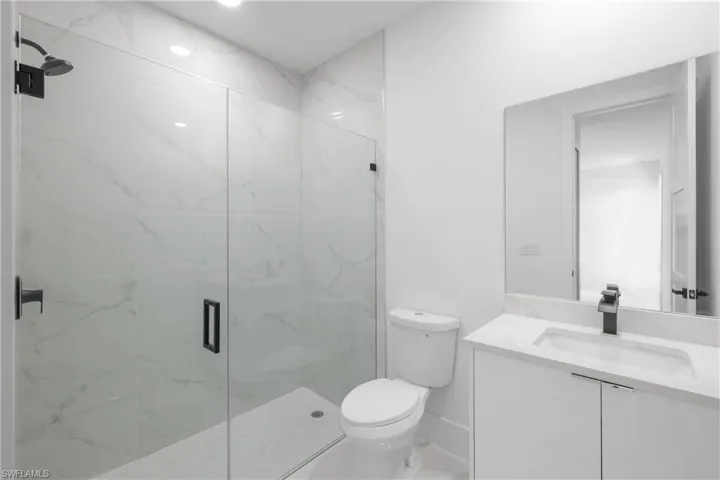 Bathroom featuring a shower with door, vanity, and toilet