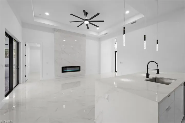 Kitchen with light stone counters, a raised ceiling, a kitchen island with sink, sink, and decorative light fixtures