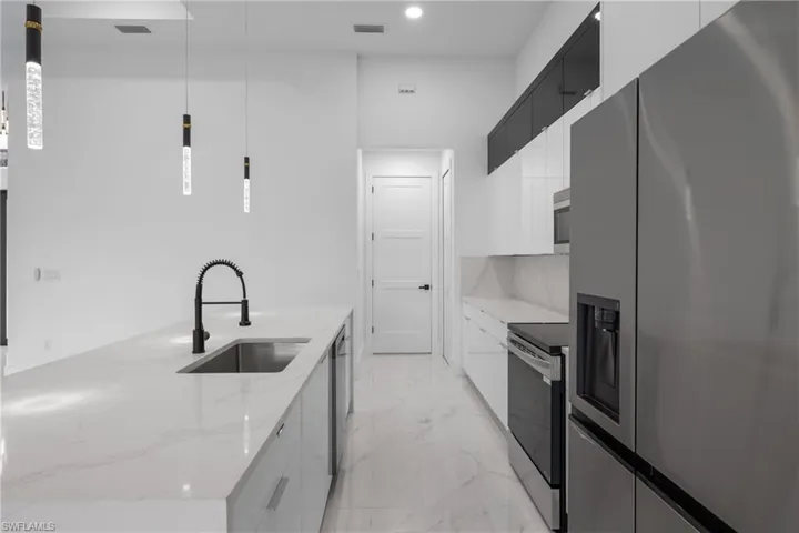 Kitchen featuring hanging light fixtures, sink, white cabinets, appliances with stainless steel finishes, and light stone counters