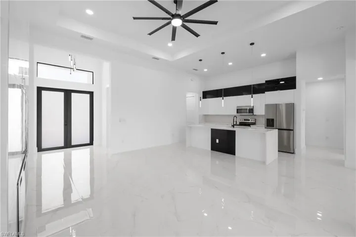 Kitchen with stainless steel appliances, decorative light fixtures, a raised ceiling, and a kitchen island with sink