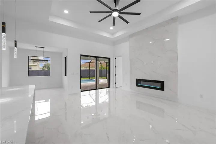 Unfurnished living room with a high end fireplace, a tray ceiling, and ceiling fan