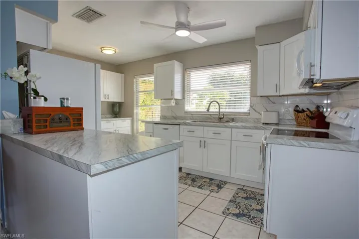 Kitchen with light tile patterned flooring, sink, white cabinetry, white appliances, and backsplash