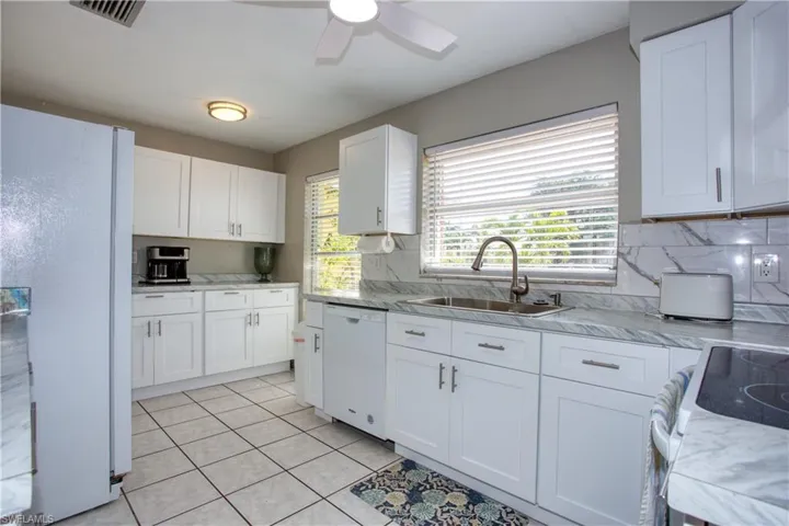 Kitchen with sink, white appliances, light tile patterned floors, white cabinetry, and decorative backsplash