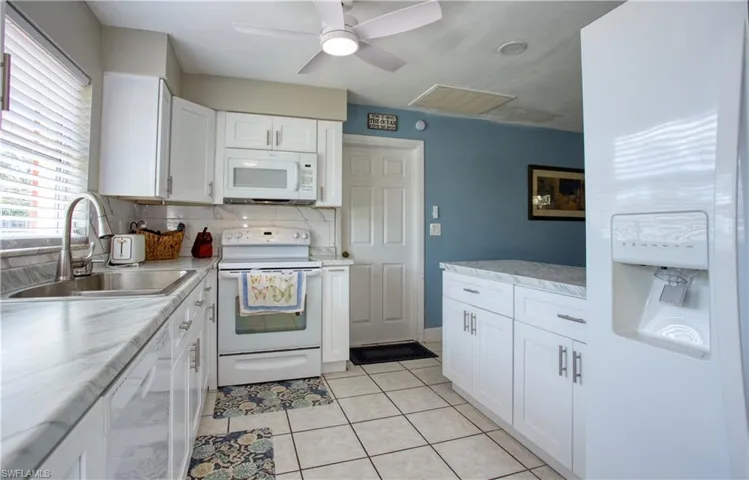 Kitchen with sink, white appliances, light tile patterned floors, and white cabinets