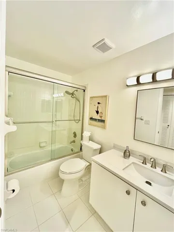 Full bath featuring vanity, tile patterned flooring, toilet, and bath / shower combo with glass door