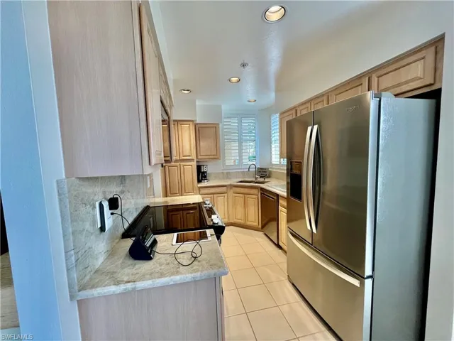 Kitchen with appliances with stainless steel finishes, a sink, light brown cabinetry, light tile patterned floors, and tasteful backsplash