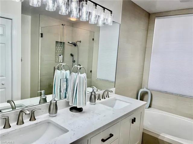 Full bathroom with a bath, a stall shower, double vanity, and tile walls
