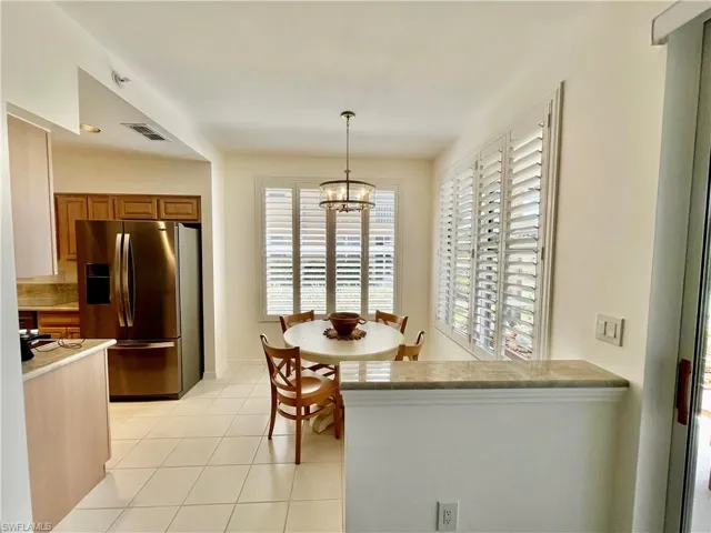 Kitchen with stainless steel fridge, brown cabinets, a chandelier, light tile patterned floors, and decorative light fixtures