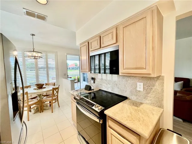 Kitchen featuring range with electric cooktop, fridge with ice dispenser, light brown cabinets, backsplash, and light countertops