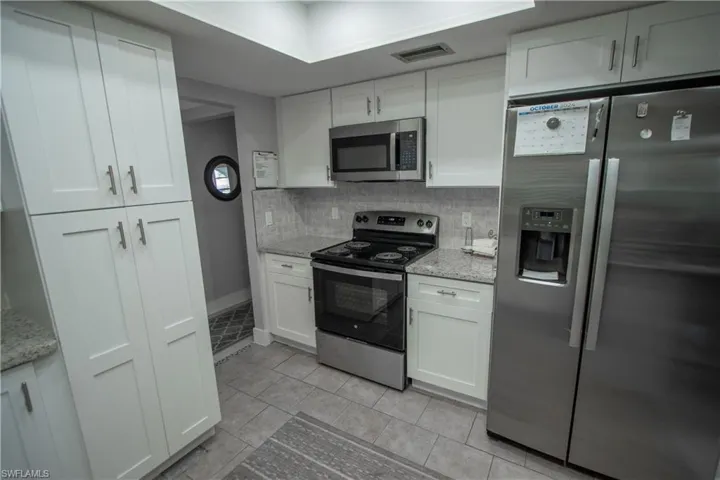Kitchen with appliances with stainless steel finishes, white cabinets, and light stone counters