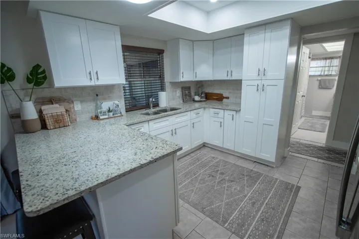 Kitchen featuring white cabinetry, sink, light stone counters, and kitchen peninsula
