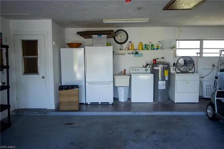 Garage featuring sink, washer and clothes dryer, electric water heater, and white fridge