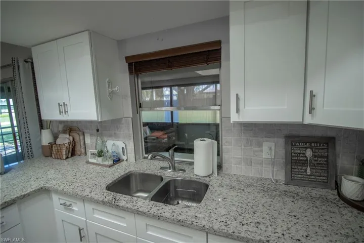 Kitchen with white cabinetry, sink, light stone countertops, and a healthy amount of sunlight