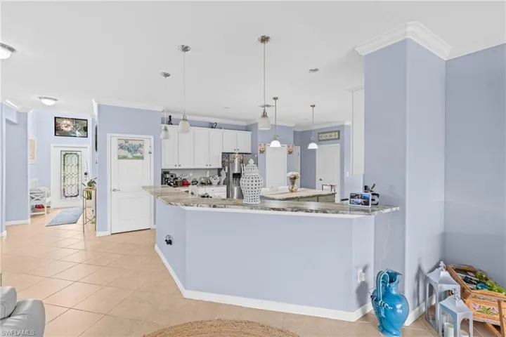 Kitchen with decorative light fixtures, ornamental molding, light stone countertops, stainless steel fridge with ice dispenser, and white cabinets