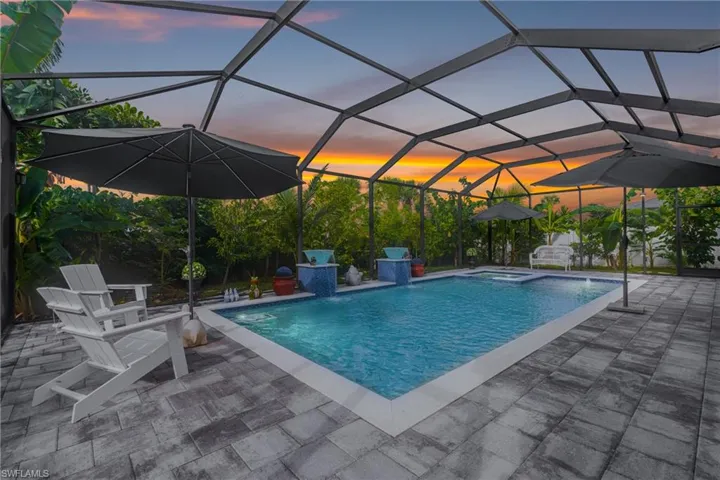 Pool at dusk with a lanai, a sunroom, a pool with connected hot tub, and a patio area