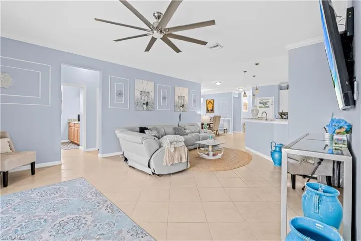 Living room featuring ornamental molding, light tile patterned flooring, and ceiling fan