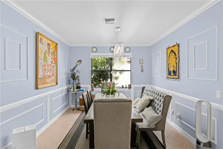 Dining space featuring a decorative wall, a chandelier, a wainscoted wall, ornamental molding, and light tile patterned floors