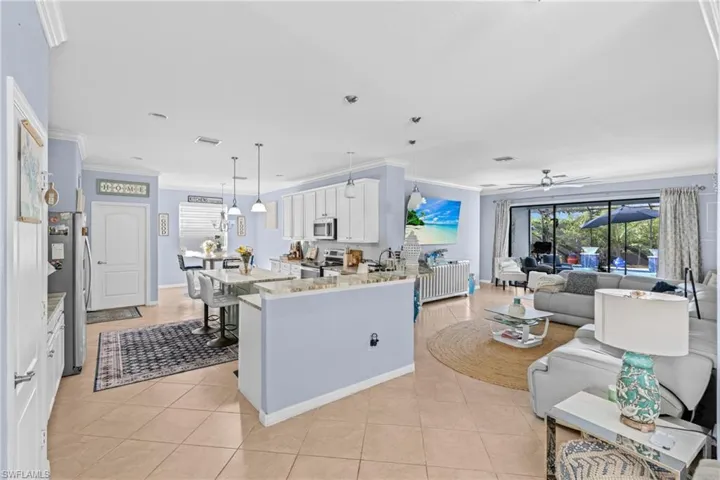 Kitchen with ornamental molding, white cabinets, light stone counters, stainless steel appliances, and decorative light fixtures