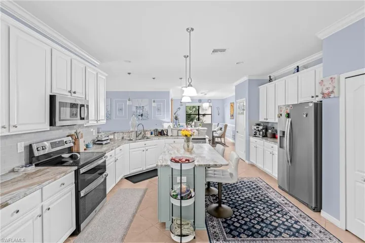 Kitchen featuring white cabinetry, stainless steel appliances, ornamental molding, a breakfast bar, and pendant lighting