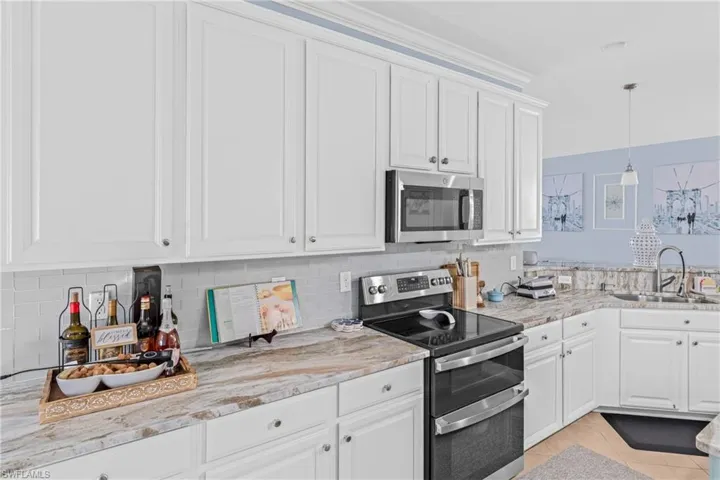 Kitchen with stainless steel appliances, white cabinets, light tile patterned floors, pendant lighting, and backsplash