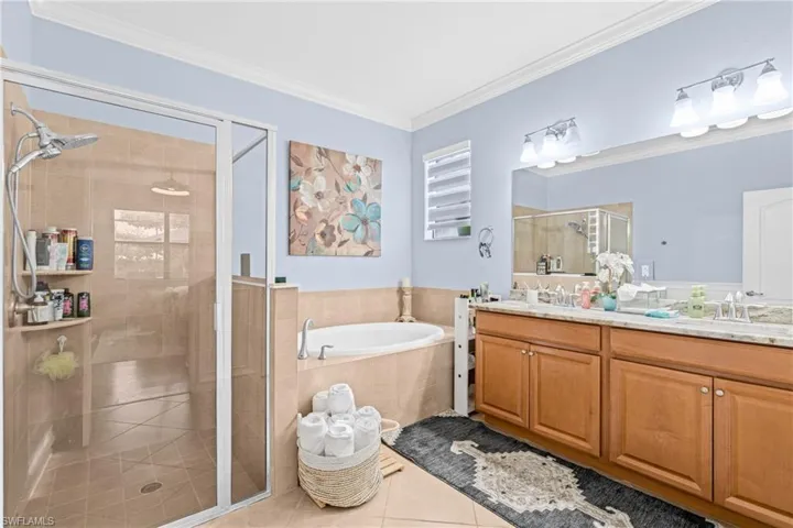 Bathroom with a shower stall, a bath, double vanity, light tile patterned floors, and crown molding