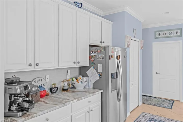 Kitchen with ornamental molding, white cabinets, stainless steel fridge, light countertops, and light tile patterned flooring