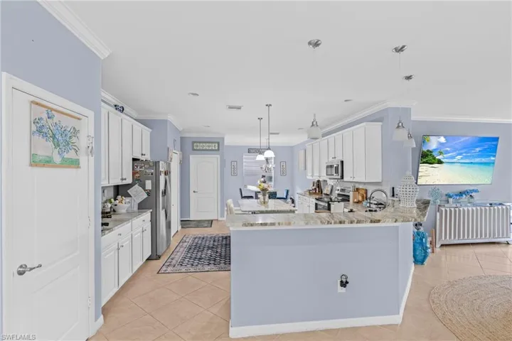 Kitchen featuring white cabinets, pendant lighting, crown molding, light stone countertops, and stainless steel appliances