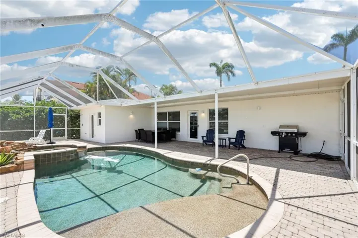 View of swimming pool featuring a patio area, grilling area, a pool with connected hot tub, and glass enclosure
